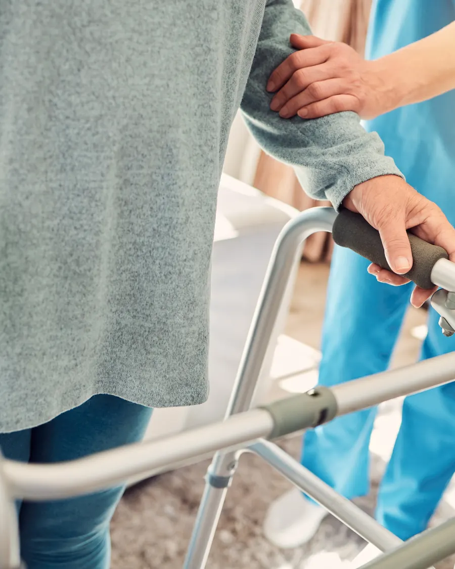 Pflegekraft unterstützt eine ältere Dame am Rollator